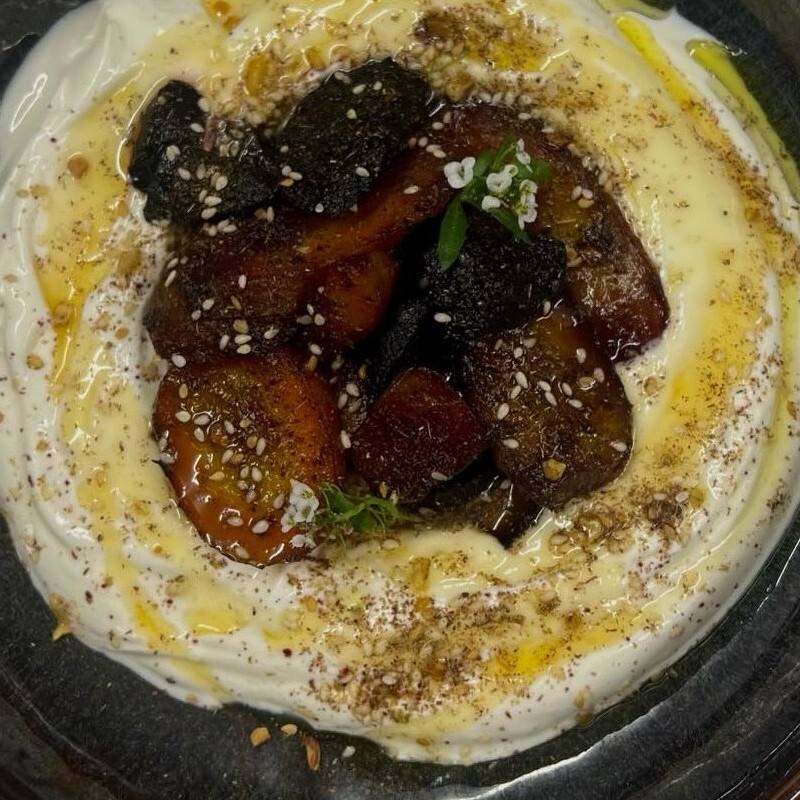 Carottes rôties posées sur le labneh, graines de sésame et dukka, dans une assiette sombre, vue du dessus.